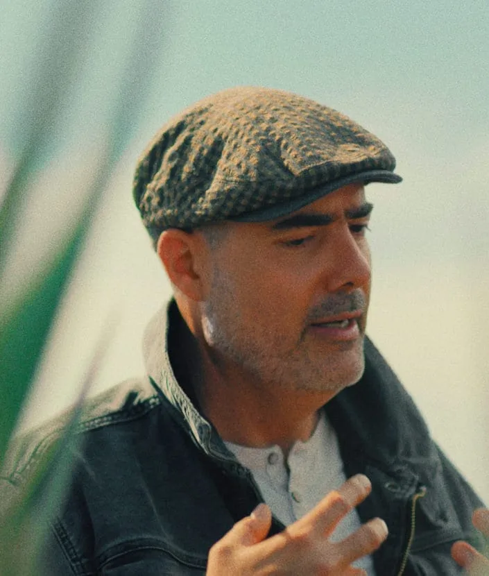 Homme portant un chapeau, faisant des gestes à l'extérieur.