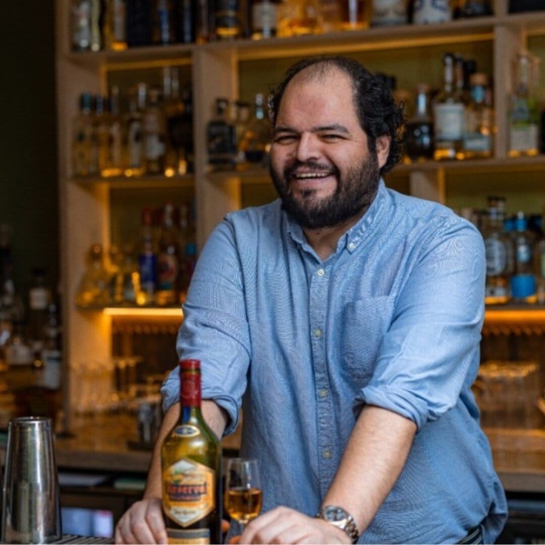 Man smiling behind bar with shelves of bottles.