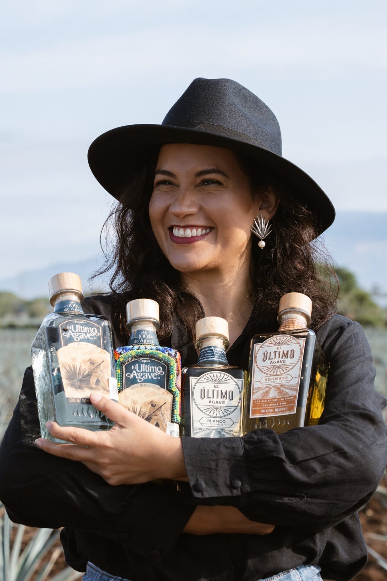 Smiling woman holds bottles of El Último Agave.