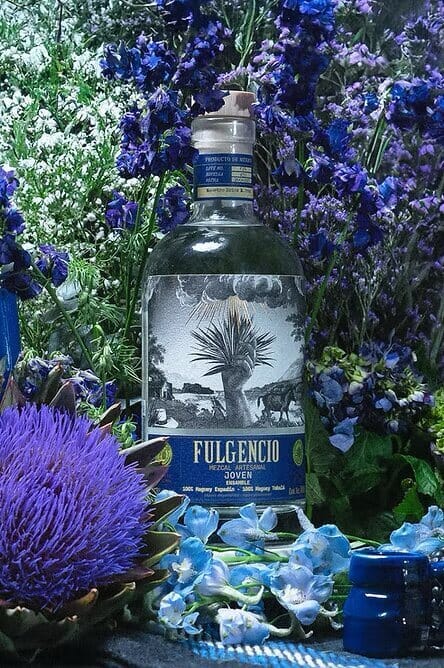 Fulgencio mezcal bottle surrounded by blue flowers